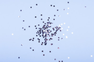 Holiday background. Group of little silver stars on blue pastel background. Top view. Copy space.