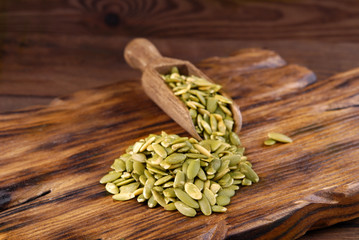 Pumpkin seeds with a bowl and scoop on a wooden background.