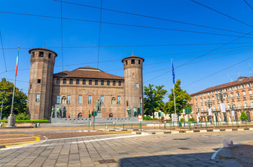 Medieval old Acaja Castle with brick towers and monuments, Prefecture building on Castle Square Piazza Castello in historical centre of Turin Torino city with clear blue sky, Piedmont, Italy