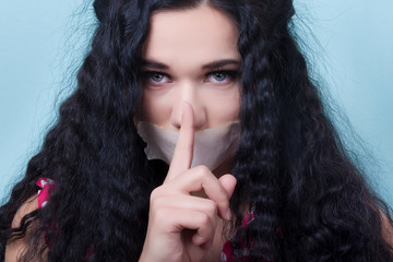 girl with a sealed mouth tape with a finger at his mouth, concept of woman restrained and abused...