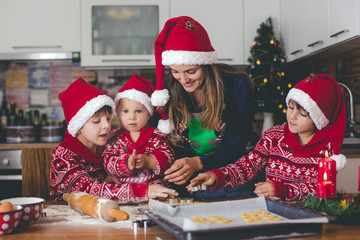 Sweet toddler child and his older brother, boys, helping mommy preparing Christmas cookies at home .