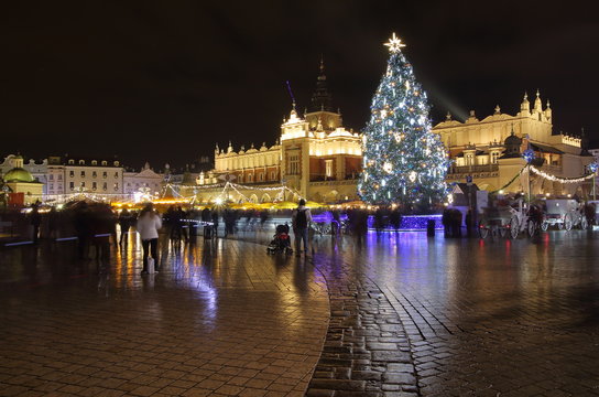 Krakow city center, Poland, main square at night decorated with beautiful huge Christams tree, buildings illuminated, nice reflections on wet ground