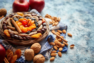 Composition of dried fruits and nuts in small wicker bowl placed on a stone table. Assortment contais almonds, walnuts, apricots, plums, figs, dates, cherries, peaches. Above view with copy space.
