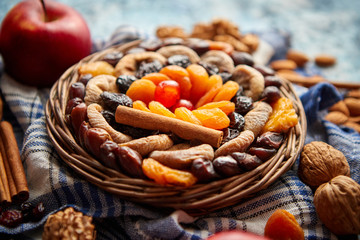 Composition of dried fruits and nuts in small wicker bowl placed on a stone table. Assortment contais almonds, walnuts, apricots, plums, figs, dates, cherries, peaches. Above view with copy space.