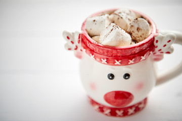Tasty homemade christmas hot chocolate or cocoa with marshmellows in a red xmas decorative cup. Placed on white wooden background.