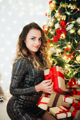 Girl in a dress near the Christmas tree with a packing box in her hands, before the new year