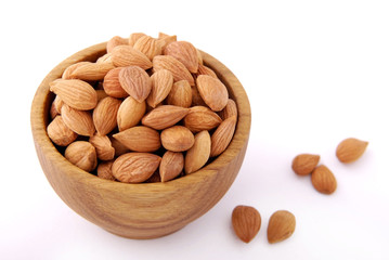 Dry apricot kernels in a wooden bowl on a white background.