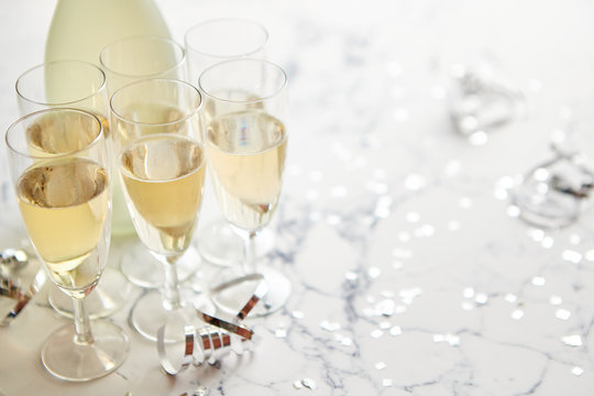 Champagne glasses and bottle placed on white marble background. Party and holiday celebration concept with confetti and serpentines. With copy space.