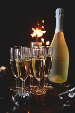 Party composition image. Glasses filled with champagne placed on black table. With bottle of wine and sparkler. Elegant composition with copy space.