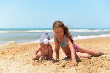 Two sisters play on a sandy beach in hot summer