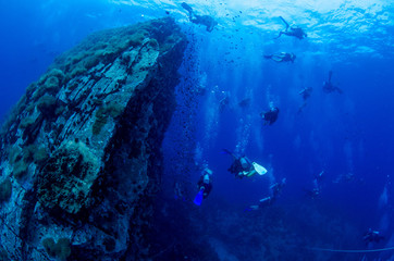 Fototapeta na wymiar Scuba divers in crystal clear water swimming around massive granite rock 