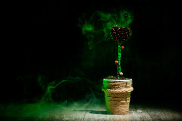 pot with decorated flower in green smoke at dark wooden background