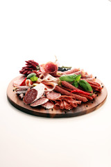 Food tray with delicious salami, pieces of sliced prosciutto crudo, sausage and basil. Meat platter with selection