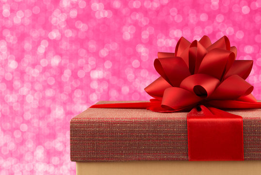 Close up on a gift box with red ribbon and bow, bokeh lights in background.