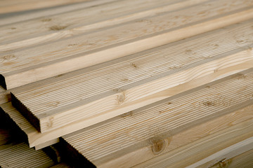 Terrace boards larch with strips, building materials in warehouse. Unpainted grooved wood terrace planks in stack.
