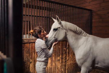 Girl jockey preparing her horse for riding in the stable