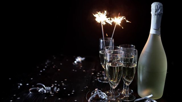 Party composition image. Glasses filled with champagne placed on black table. With bottle of wine and sparkler. Elegant composition with copy space.
