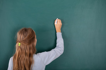 Female Student Writing With Chalk On Chalkboard