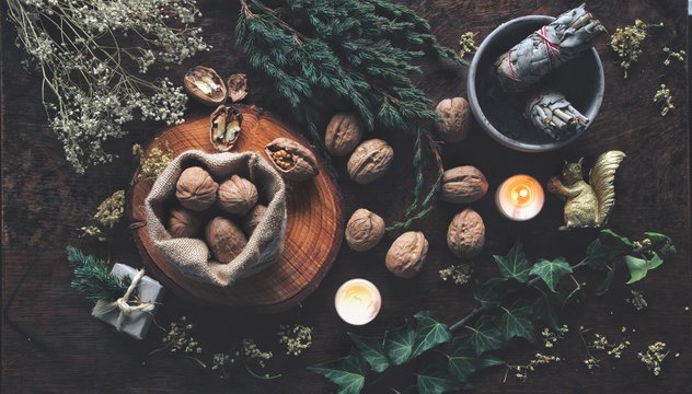 Walnuts in small brown sack and all over wiccan witch altar as method of  divination for Yule winter solstice (Christmas) time. Flat lay with evergreen ivy branches, dried flowers, sage in background