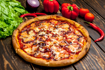 pizza on wooden table with ingredients, tomatoes, pepper, onion