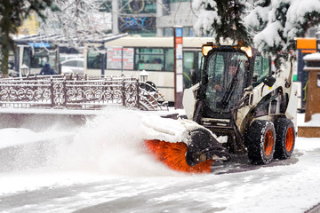 City service cleaning snow , a small tractor with a rotating brush clears a  road in the city park...