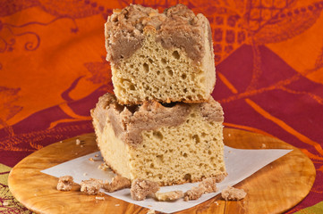 Top, front, close distance of two stacked squares of freshly baked, homemade, crumb coffee cake on a square, white plate with a print, cloth napkin