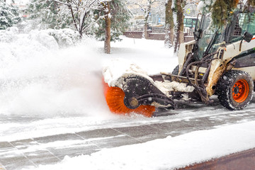 City service cleaning snow , a small tractor with a rotating brush clears a  road in the city park...