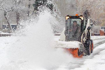 City service cleaning snow , a small tractor with a rotating brush clears a  road in the city park