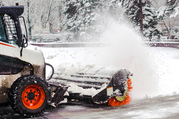 City service cleaning snow , a small tractor with a rotating brush clears a  road in the city park...
