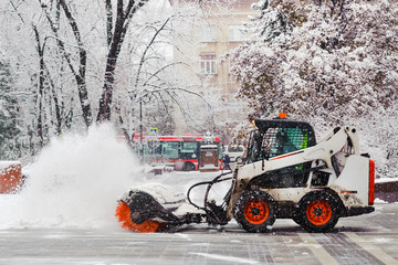 City service cleaning snow , a small tractor with a rotating brush clears a  road in the city park