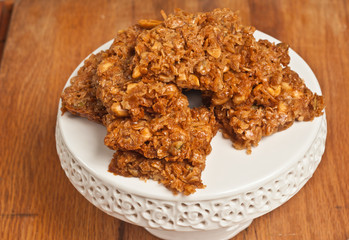 Top view, close up of seven, freshly baked, homemade, peanut coconut bars on a white, round,  pedestal,  display dish on a wood cutting board