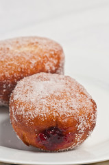 Top view, close up of two , freshly baked, homemade raspberry jelly filled donuts , sprinkled, with cane sugar on a white, round plate