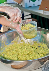 front view, close distance of the arm and hand of a male vendor scooping out guacamole into a plastic container, to sell at a tropical farmers market on a sunny, winter day