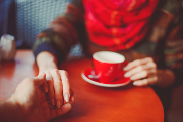 Young couple drinking coffee in a bar cafe - male hand holding female hand - concept of couple in love, trust and friendship