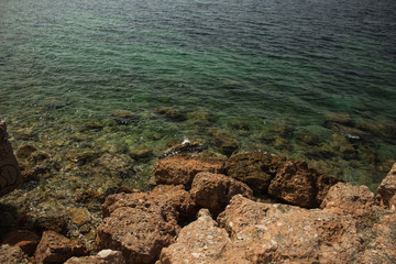 Fototapeta na wymiar rock sea shore waterfront line with underwater stones in transparent green water surface Mediterranean landscape