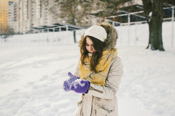 Portrait of a beautiful young Caucasian woman in a knitted hat and scarf standing on a winter background with snow smile and happiness purple gloves sculpt a snowball