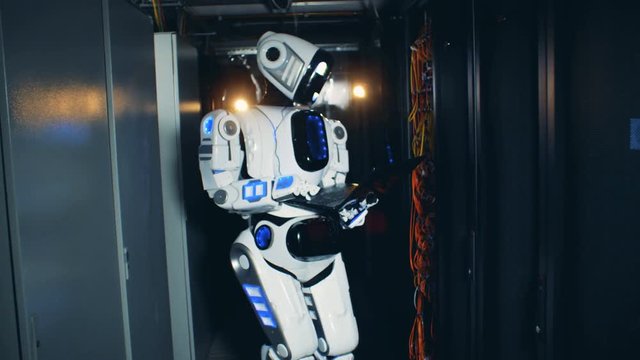 White droid working with a laptop at a data center, close up.