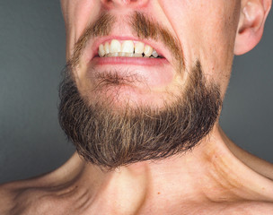 Male with nicely trimmed beard, showing teeth in anger and flexing neck muscles