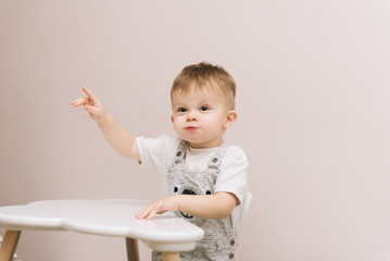 Fototapeta premium Cute baby sitting at the table and shows his finger in the nursery bright colors.