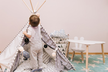 Cute baby playing with a wigwam tent in the children's room in bright colors. © ksyusha_yanovich