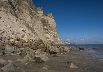 Fototapeta na wymiar Rocks cover the sand beach below jagged cliffs along the sea in New Zealand