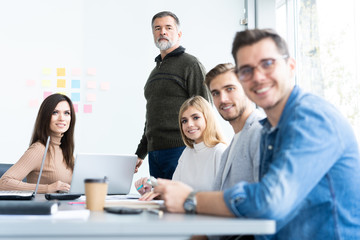 Enjoying his work. Handsome young man looking at camera and smiling while his colleagues working in the background.