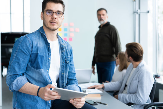 Young and creative. Handsome young man holding digital tablet and smiling while his colleagues discussing something in the background.