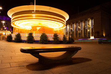 Christmas fairground ride in the city at night on a bench and spinning carousel