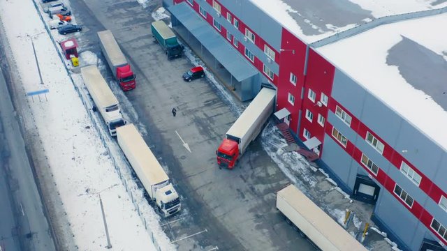 Aerial circling view of semi-trailer truck standing on the load/unload goods at the warehouse logistic center on winter day