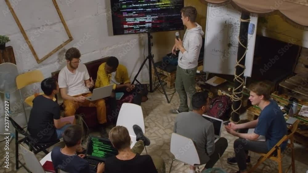 Poster high angle view of group of multiethnic young people sitting on chairs and doing coding task during 