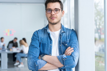 Smiling businessman in denim shirt and eyeglasses looking at camera in office.