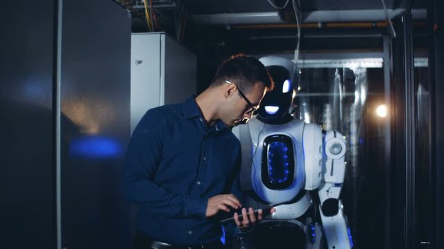 Man and robot walk in a server room, close up.
