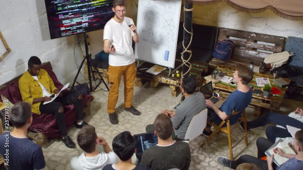 Poster high angle view of young man in casual clothes delivering presentation about coding, group of divers