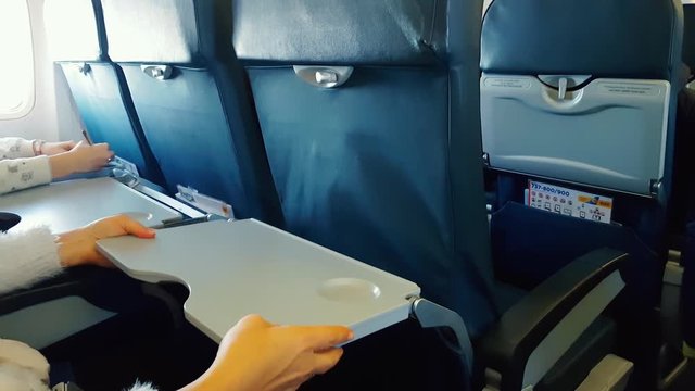 The girl opens a table in the plane, the passenger in the plane